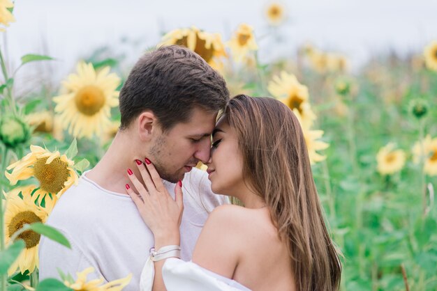 Liebevolles Paar in weißen Kleidern, die sich küssen, lächeln und in einem Feld von Sonnenblumen umarmen