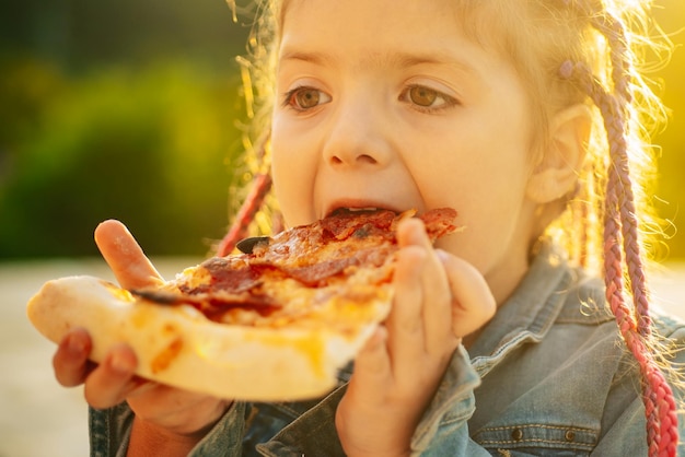 Lieblingsessen der Kinder. Leckere Pizza. Kind isst Pizza. Fastfood. Italienisches Junkfood. Mittagessen des kleinen Mädchens im Freien.