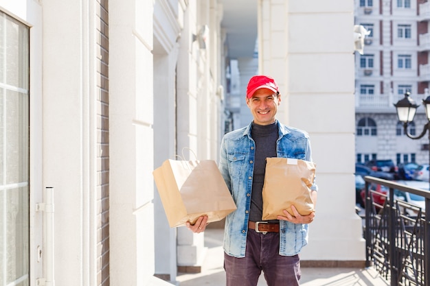 Liefer-, Post- und Personenkonzept - Mann, der Kaffee und Essen in Einweg-Papiertüten zum Kunden nach Hause liefert