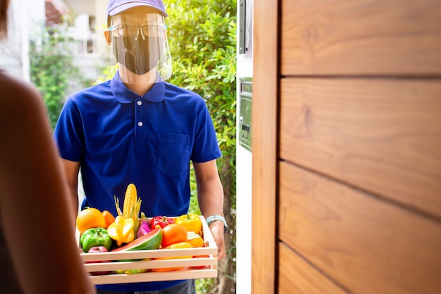 Lieferasiatischer Mann, der frisches Gemüse und Obst in einer Kistenbox hält, bereiten den Kunden zu Hause vor