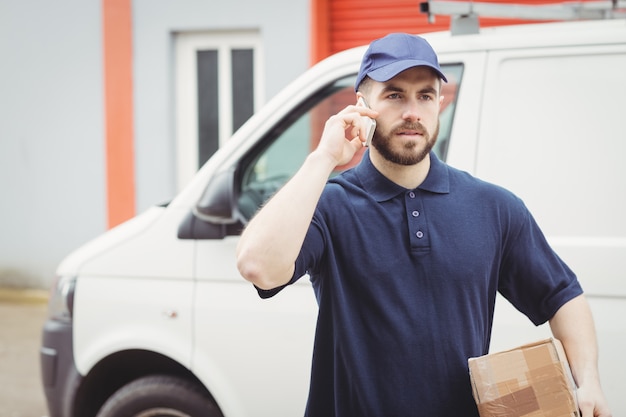 Lieferbote, der einen Telefonanruf beim Halten eines Pakets macht