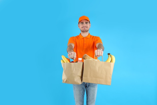 Lieferbote hält Taschen mit Lebensmitteln auf blauem Hintergrund