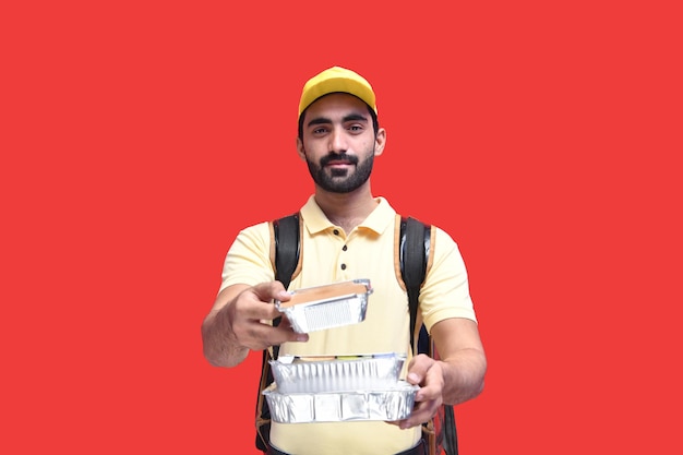 Lieferbote in gelbem T-Shirt und Mütze mit Rucksack mit Essen zum Mitnehmen indisches pakistanisches Modell