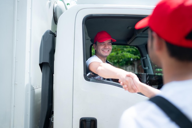 Lieferbote mit roter Mütze und Uniform schüttelt sich gegenseitig die Hand, nachdem er die Lieferungen beendet hat