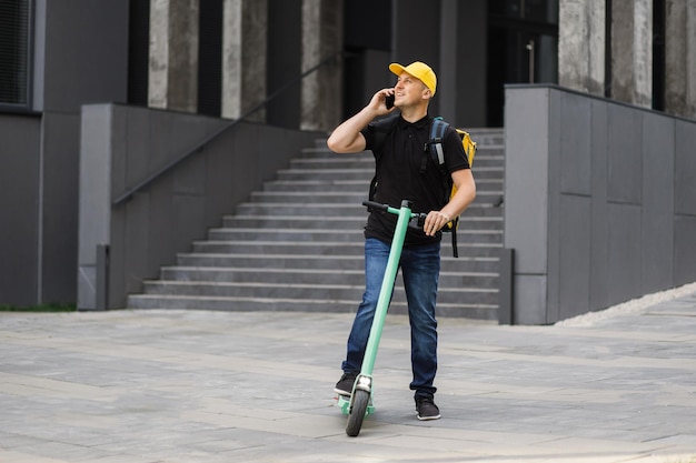 Lieferbote mit Smartphone und Push-Scooter in der Stadt