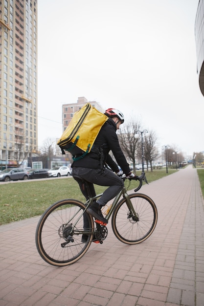 Lieferbote trägt Helm und Thermo-Rucksack und fährt während der Arbeit Fahrrad