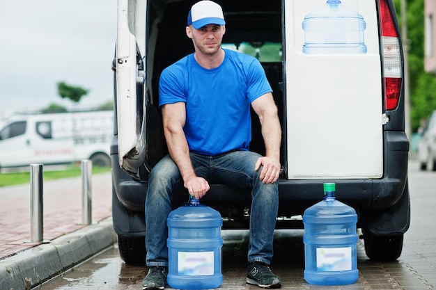 Foto lieferbote vor dem lieferwagen, der wasserflaschen liefert.