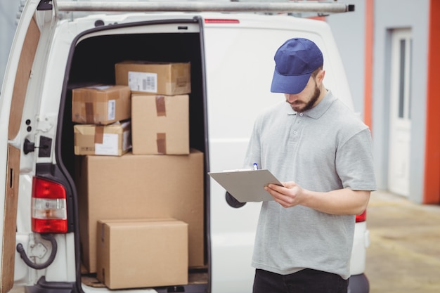 Lieferboteschreiben auf Klemmbrett vor seinem Packwagen