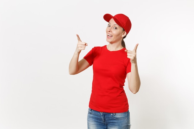 Lieferfrau in der roten Uniform lokalisiert auf weißem Hintergrund. Professionelle kaukasische Frau in Mütze, T-Shirt, Jeans, die als Kurier oder Händler arbeitet und Zeigefingerkamera auf Kopienraumwerbung zeigt