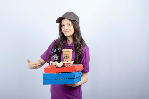 Lieferfrau in lila Uniform mit Pizzaschachteln und Kaffeetassen. Hochwertiges Foto