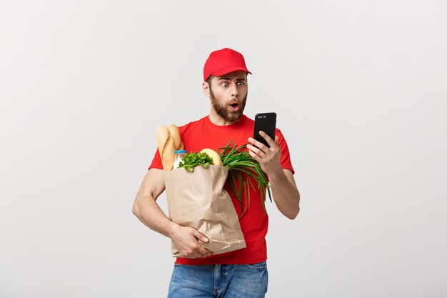 Lieferkonzept: Hübscher kaukasischer Kuriermann der Lebensmittellieferung in roter Uniform mit Einkaufsbox
