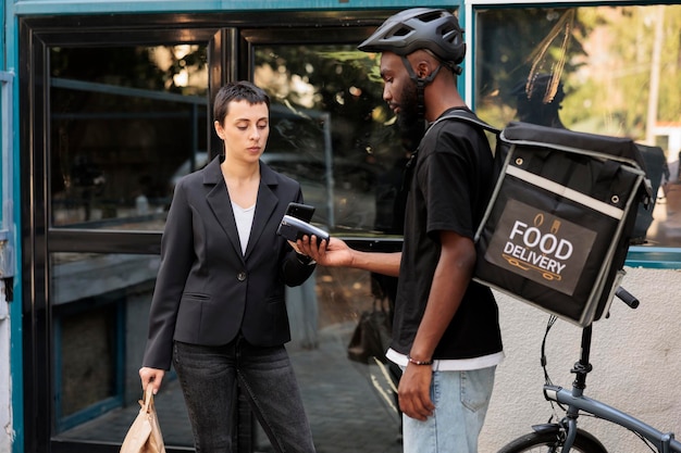 Lieferservice für Lebensmittel im Büro, Zahlung per Smartphone-POS-Terminal, Frau, die mit mobiler Brieftasche für das Mittagessen bezahlt. Kurier, der Mitarbeiter des Restaurants zum Mitnehmen vor dem Firmengebäude liefert