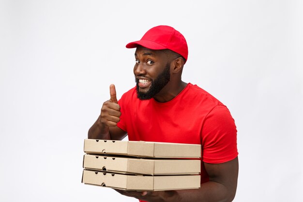 Lieferservice - Porträt eines glücklichen afroamerikanischen Lieferers, der ein Pizzaschachtelpaket hält und Daumen hoch zeigt.