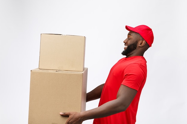 Lieferservice - Seitenansicht Porträt eines glücklichen afroamerikanischen Lieferers in rotem Stoff, der ein Kastenpaket hält.