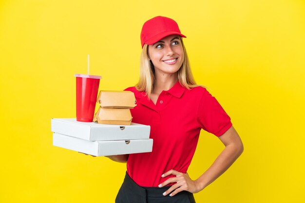 Lieferung Uruguayische Frau, die Fast Food isoliert auf gelbem Hintergrund hält und eine Idee denkt, während sie nach oben schaut