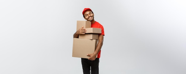 Lieferungskonzept Porträt eines glücklichen afroamerikanischen Lieferers in rotem Tuch, der ein Kartonpaket hält, das auf grauem Studio-Hintergrund-Kopienraum isoliert ist
