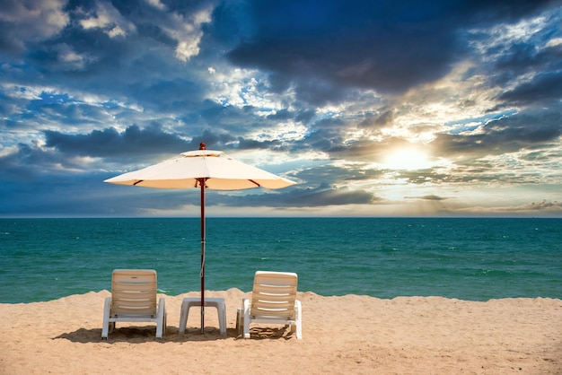 Liegestühle am Sandstrand mit dramatischem Himmel bei Sonnenuntergang