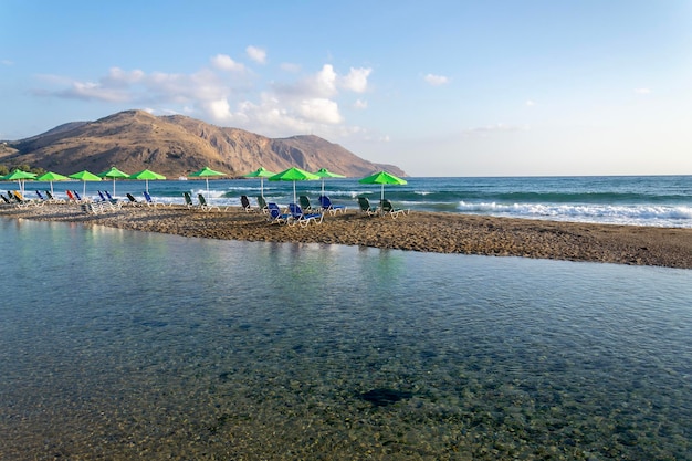 Liegestühle am Strand unter Sonnenschirmen auf der sandigen Halbinsel zwischen Meer und Fluss in der Nähe von Georgioupolis Kreta