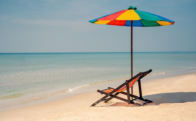 Liegestuhl mit farbenfrohem Sonnenschirm, tropischem Sandstrand, Sommerreiseurlaub und Sommerurlaubskonzepten