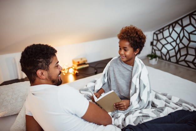 Lies mir eine Gutenachtgeschichte. Kleines Mädchen und ihr Vater auf dem Bett zu Hause.