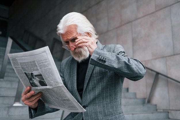 Liest Zeitung Älterer Geschäftsmann in formeller Kleidung mit grauem Haar und Bart ist im Freien