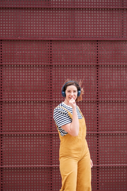 Lifestyle-Frau mit gelben Latzhosen, die auf rotem Hintergrund singen Konzept Freiheit Spaß im Freien