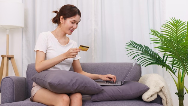 Lifestyle im Wohnzimmerkonzept Asiatische Frau mit Kreditkarte und Laptop zum Online-Shopping