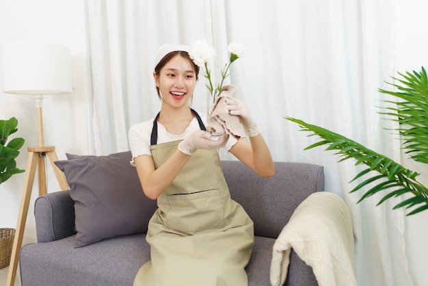 Lifestyle im Wohnzimmerkonzept Junge Asiatin im Handschuh mit Tuch zum Abwischen der Blumenvase