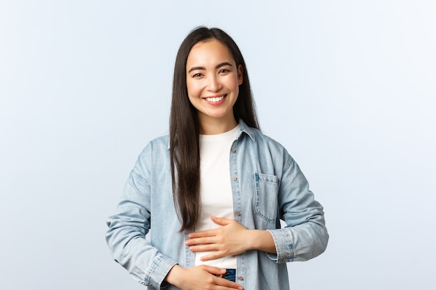 Lifestyle, Menschen Emotionen und Schönheitskonzept. Erfreut lächelnde asiatische Frau, die sich den Bauch reibt, nach dem Essen voll ist, zufriedenes Gefühl im Magen vom Trinken von Joghurt