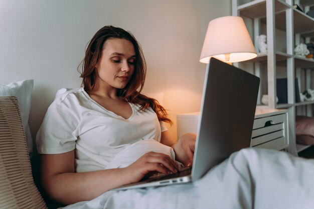 Lifestyle-Momente einer jungen Frau zu Hause. Frau, die vor dem Schlafengehen am Laptop arbeitet