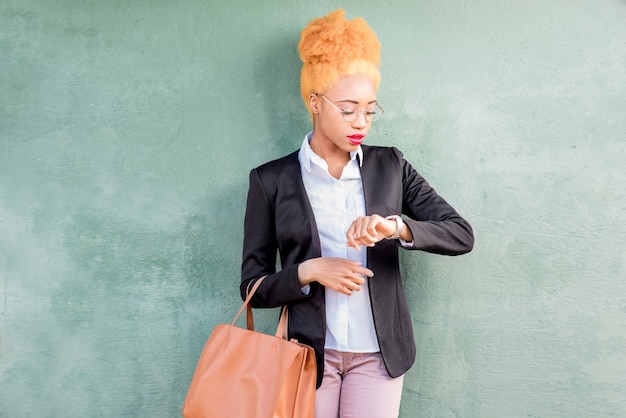Lifestyle-Porträt einer afrikanischen Geschäftsfrau im Freizeitanzug mit Tasche auf dem grünen Wandhintergrund