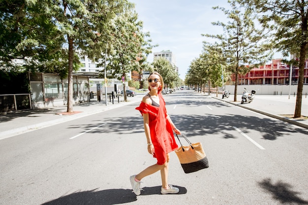 Lifestyle-Porträt einer Frau im roten Kleid, die die Straße im modernen Stadtteil Barcelona überquert?
