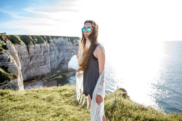 Lifestyle-Porträt einer jungen Frau im Hippie-Stil, die die Natur an der felsigen Küste mit herrlichem Blick auf das Meer in Frankreich genießt