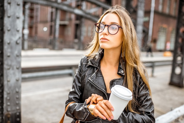 Lifestyle-Porträt einer stilvollen Geschäftsfrau, die die Zeit im Freien mit Kaffeetasse auf der Eisenbrücke überprüft