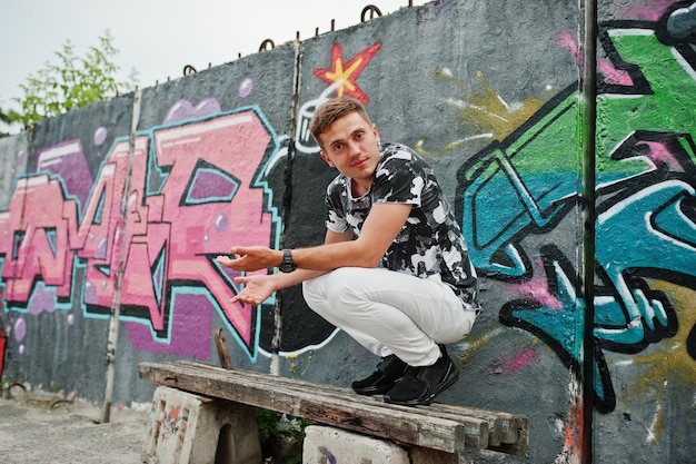 Lifestyle-Porträt eines gutaussehenden Mannes, der auf der Straße der Stadt mit Graffiti-Wand posiert