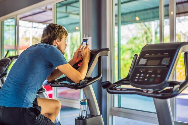 Foto lifestyle-porträt eines gutaussehenden mannes mit telefon, der auf dem simulator im fitnessstudio sitzt