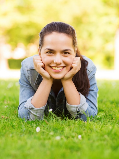 Lifestyle, Sommerurlaub, Freizeit und Personenkonzept - lächelndes junges Mädchen, das auf Gras im Park liegt