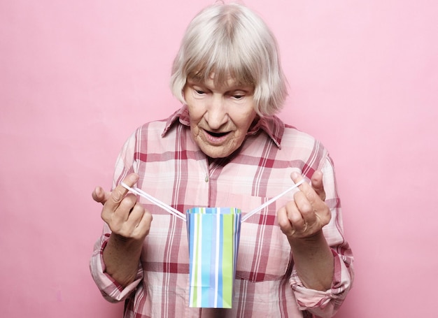 Foto lifestyle- und people-konzept glückliche seniorin mit einkaufstasche auf rosafarbenem hintergrund