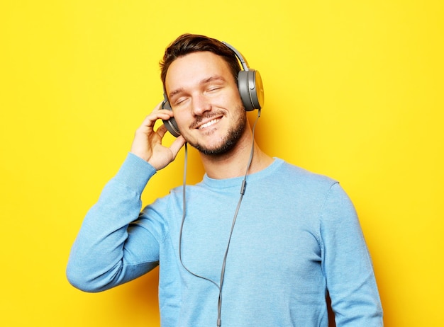 Lifestyle- und People-Konzept Junger Mann mit Kopfhörern und Handy auf gelbem Hintergrund