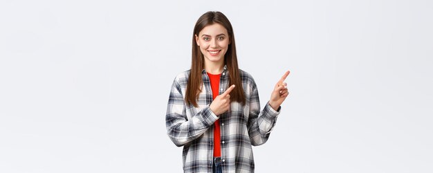 Lifestyle verschiedene Emotionen Freizeitaktivitäten Konzept Freundlich aussehendes attraktives kaukasisches Mädchen in kariertem Hemd informieren über neue Promos, die mit dem Finger nach rechts zeigen und die Kamera lächeln