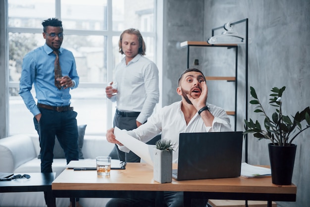 Ligar para um funcionário. Líderes de equipe têm humor bem-sucedido no local de escritório com janela no fundo