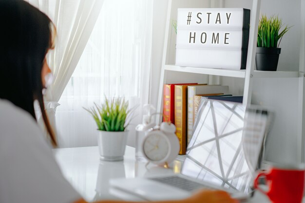 Lightbox con el hashtag de texto #STAYHOME brillando en la luz y borrosa mujer que trabaja en casa. Oficinista en cuarentena. Inicio trabajando para evitar la enfermedad viral. Concepto de trabajador independiente o remoto.