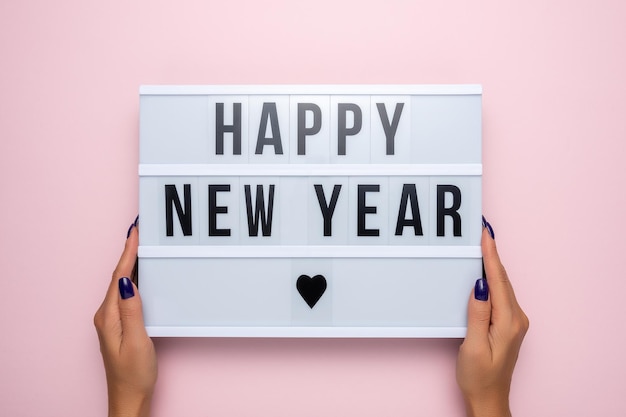 Lightbox con el texto FELIZ AÑO NUEVO en manos de mujeres sobre un fondo rosa