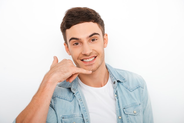 Ligue-me a qualquer hora! Jovem feliz gesticulando e sorrindo em pé contra um fundo branco