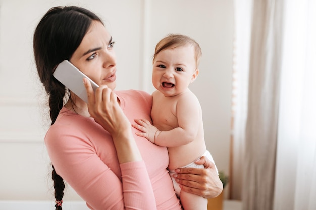 Ligue para o pediatra preocupado com a jovem mãe chateada com o bebê chorando falando ao telefone com o médico e