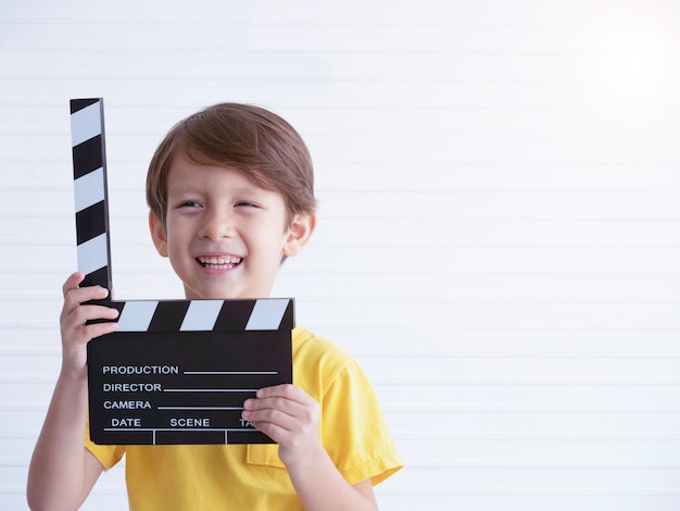 Foto liitle kaukasischer junge, der film hält, das klappbrett mit lächeln macht.