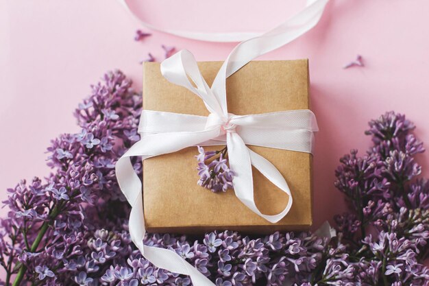 Lila Blumen und Geschenkbox auf rosafarbenem Papier Draufsicht Glücklicher Muttertag und Frauentag