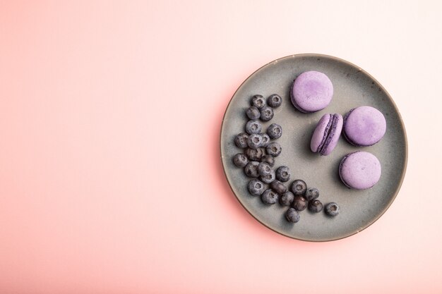 Lila Macarons oder Macaroons-Kuchen mit Blaubeeren auf Keramikplatte auf einem pastellrosa Hintergrund.