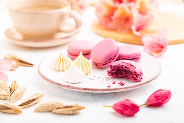 Lila Macarons oder Macaroons-Kuchen mit Tasse Kaffee auf einem weißen Betonhintergrund, der mit Blumen verziert wird.