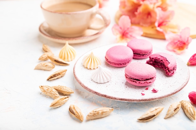 Lila Macarons oder Makronenkuchen mit Tasse Kaffee auf einem weißen Betonhintergrund, der mit Blumen verziert wird. Seitenansicht,